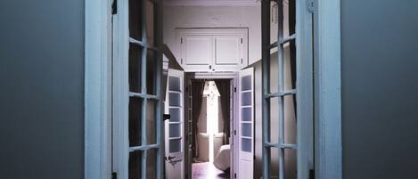 A narrow hallway with open doors leading to a bedroom.