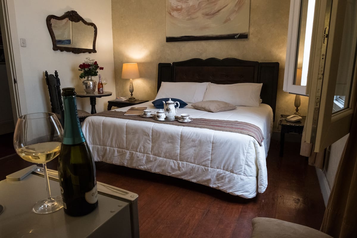 Ein Hotelzimmer mit Bett, Nachttisch, Lampe und einer Weinflasche.