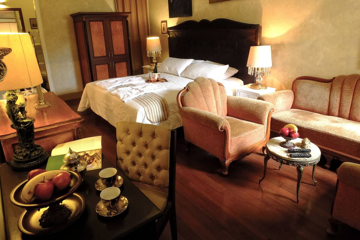 Ein Hotelzimmer mit einem Bett, zwei Sesseln, einem kleinen Tisch mit Obstschale und einem Schreibtisch mit Lampe.