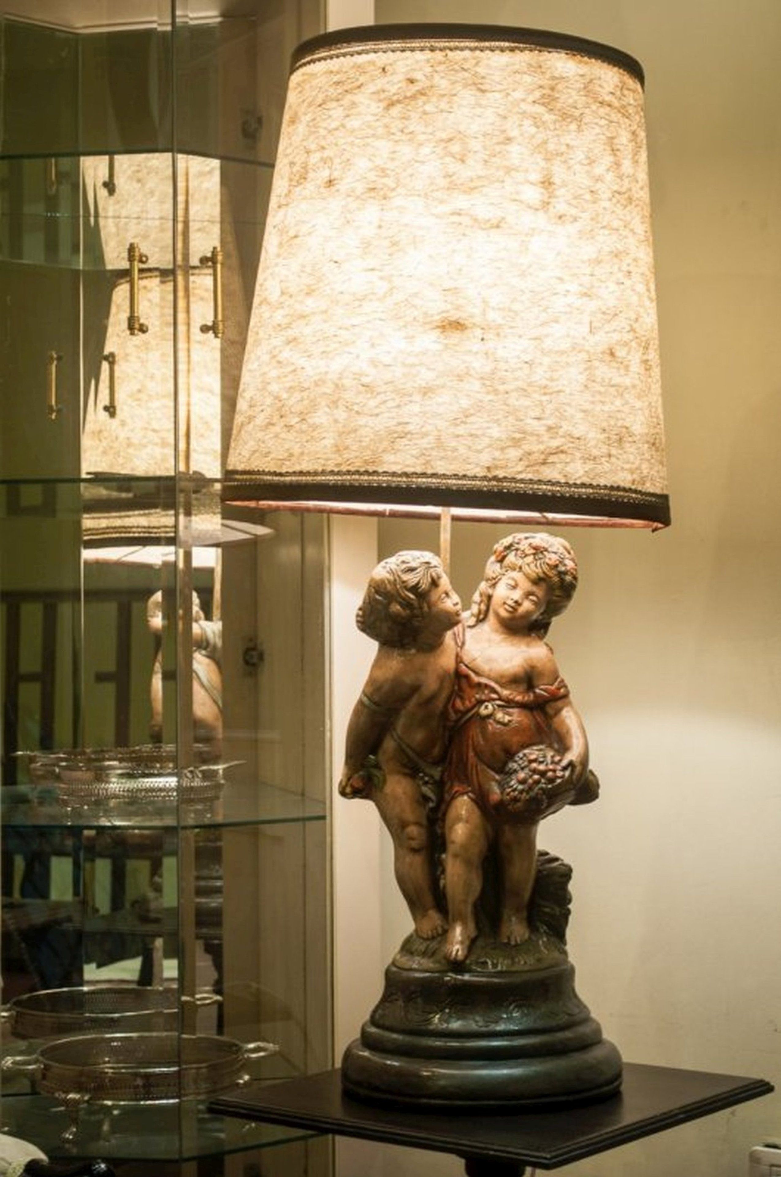 A table lamp with a textured shade and a base featuring a sculpture of two figures.