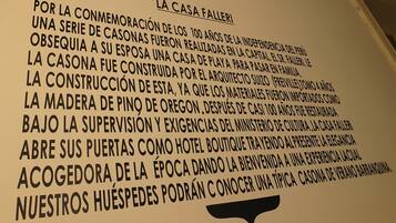 A sign with text about La Casa Falleri, a building commemorating 100 years of Peruvian independence, constructed by architect Suizo, made of Oregon pine wood, and now functioning as a hotel boutique.
