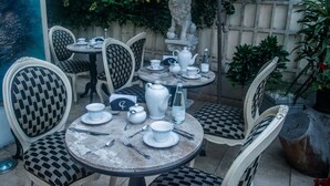 Eine Terrassenanlage mit runden Tischen und karierten Stühlen, ausgestattet mit Teesets und von Grünpflanzen umgeben.