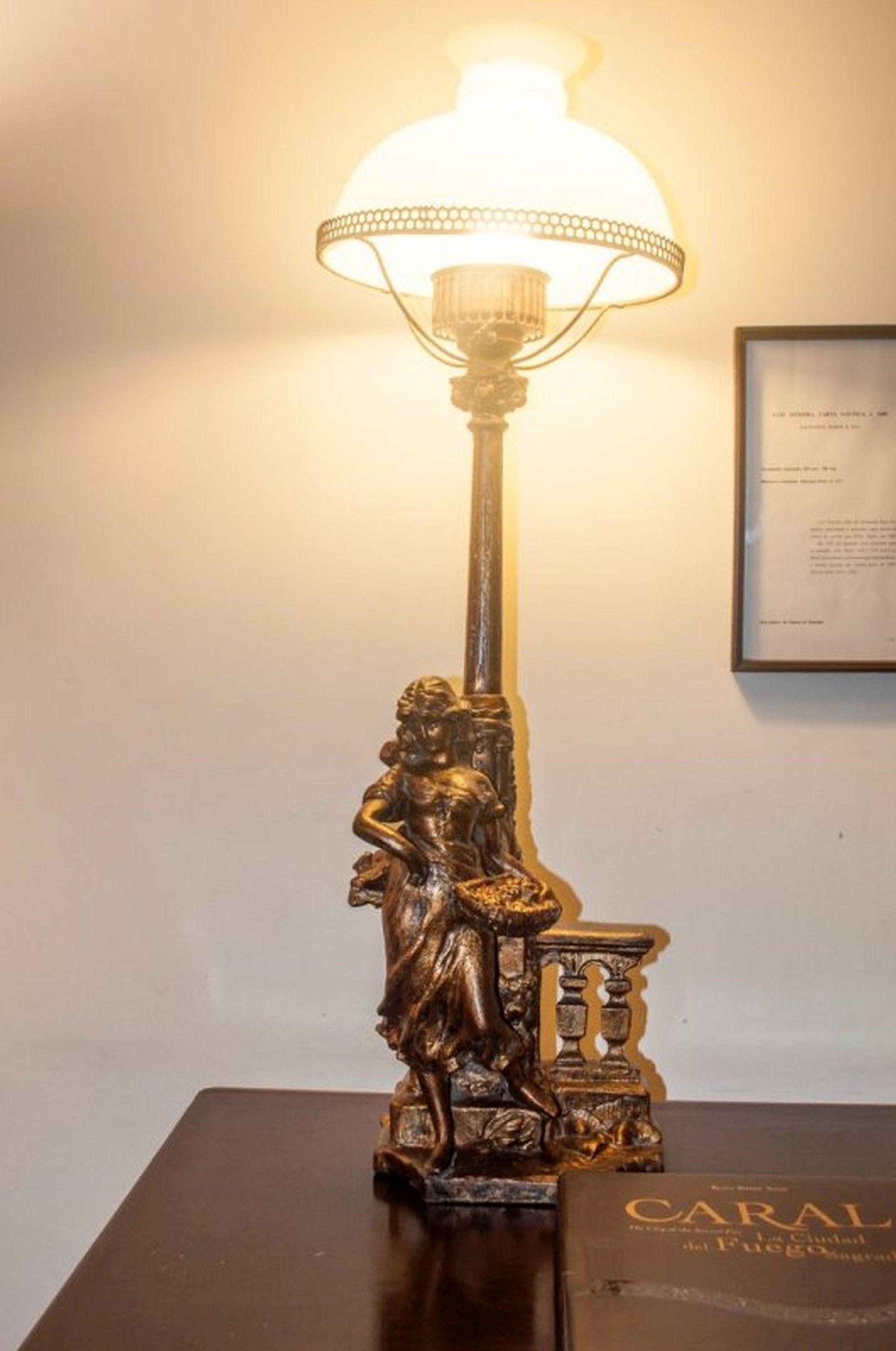 Un tavolo con una lampada, una statua di donna e un libro intitolato "CARAL".