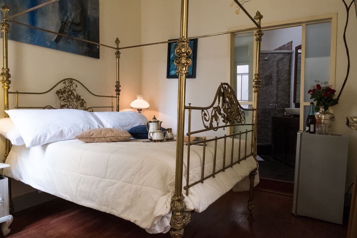Ein Hotelzimmer mit einem Himmelbett mit aufwendiger Metallverzierung, einem Nachttisch mit Lampe und einem Kühlschrank.