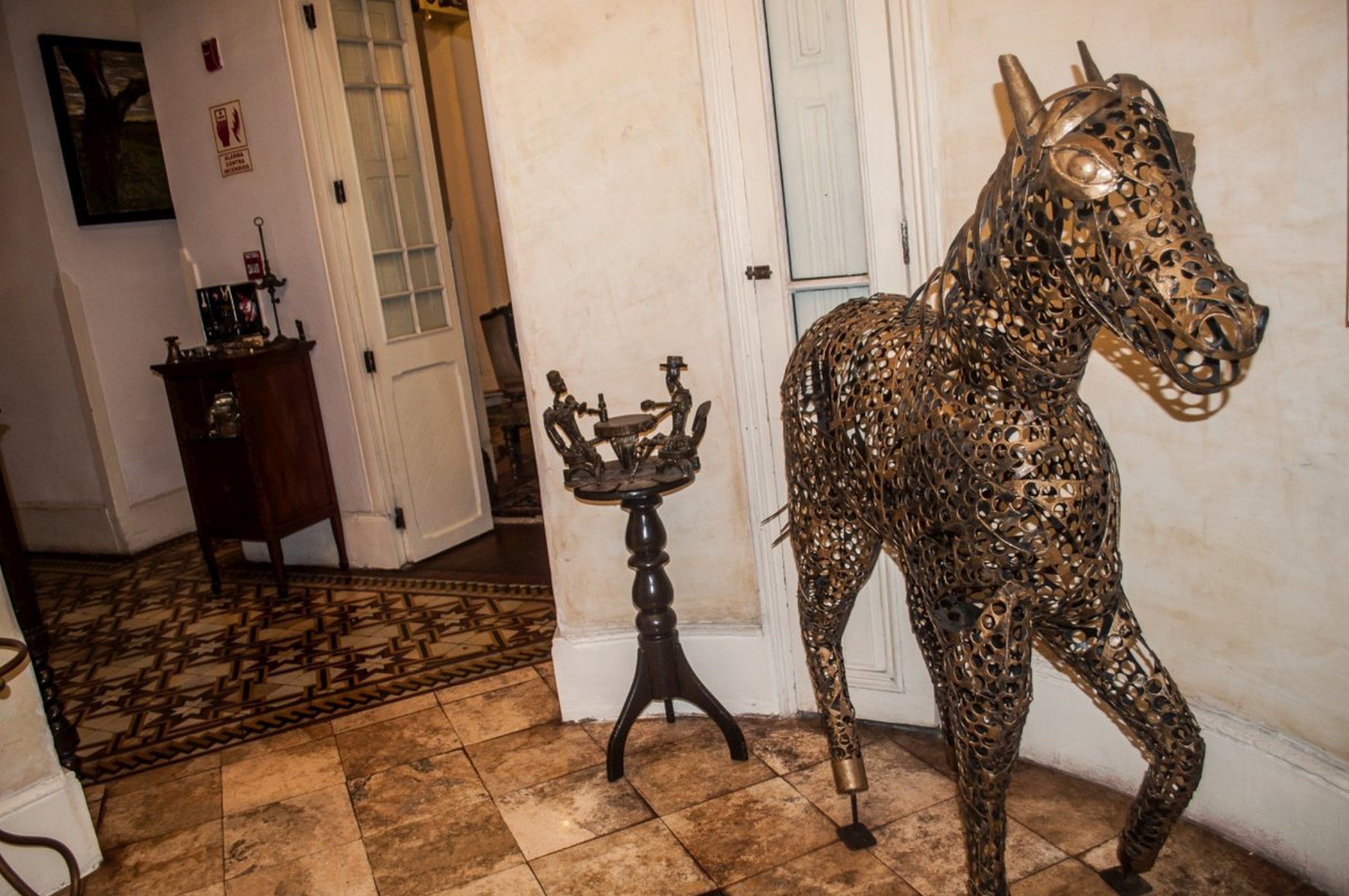 A hallway with a metal horse sculpture, a small table with a candle, and a door.