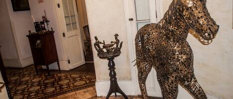 A hallway with a metal horse sculpture, a small table with a candle, and a door.
