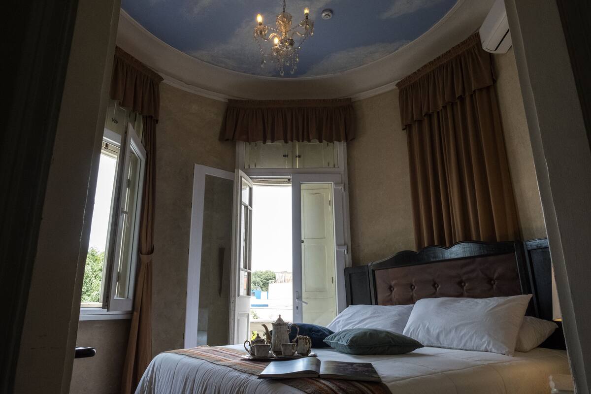 Ein Schlafzimmer mit einem großen Bett, einer Chandelieber und Blick durch eine geöffnete Tür.