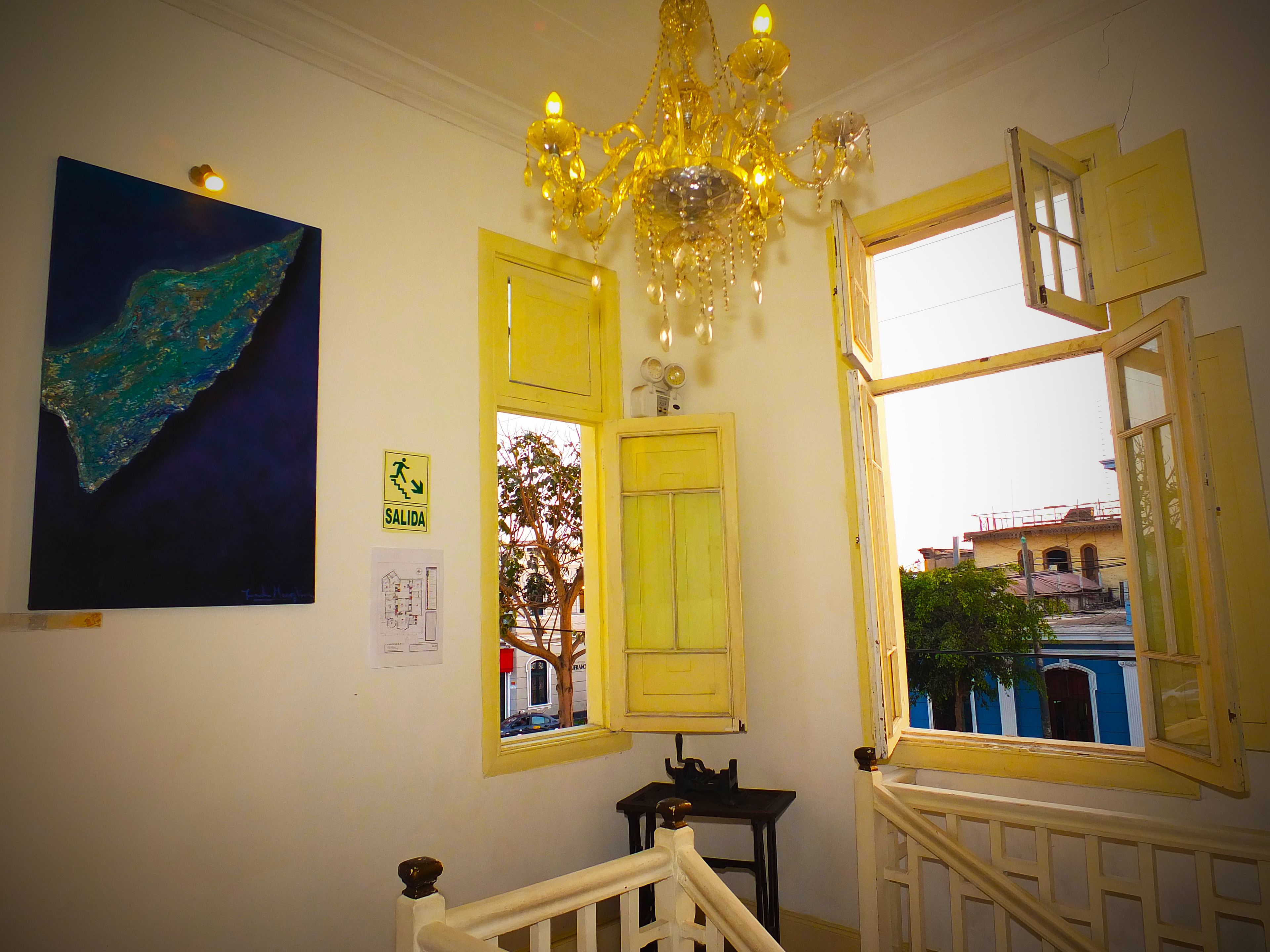 A staircase with a chandelier, a painting, and a window with a view of buildings outside.