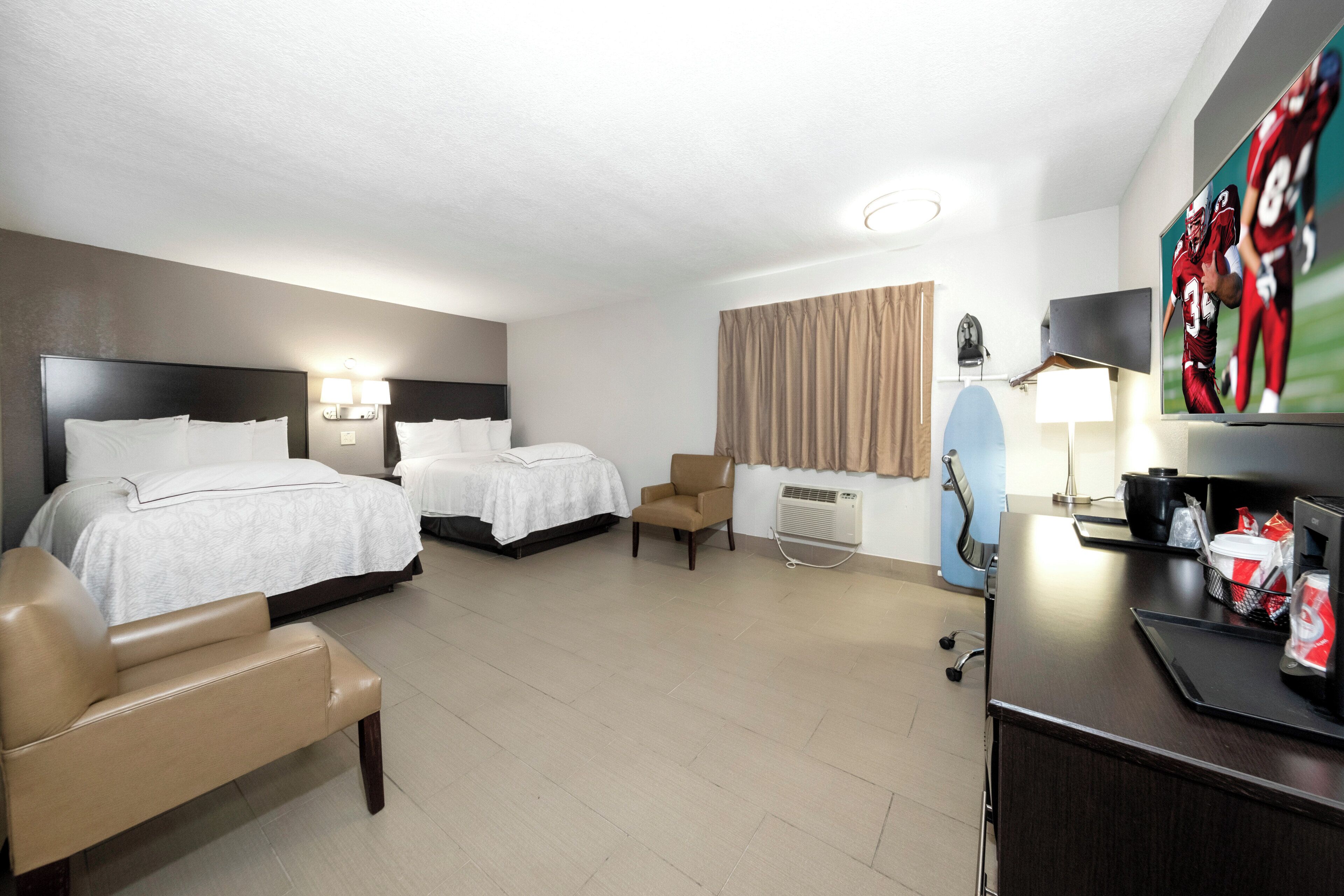 A hotel room with two beds, a desk, a chair, a TV, and a window with curtains.