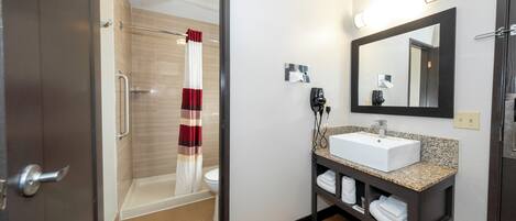 A hotel bathroom with a shower, toilet, sink, and a towel rack.