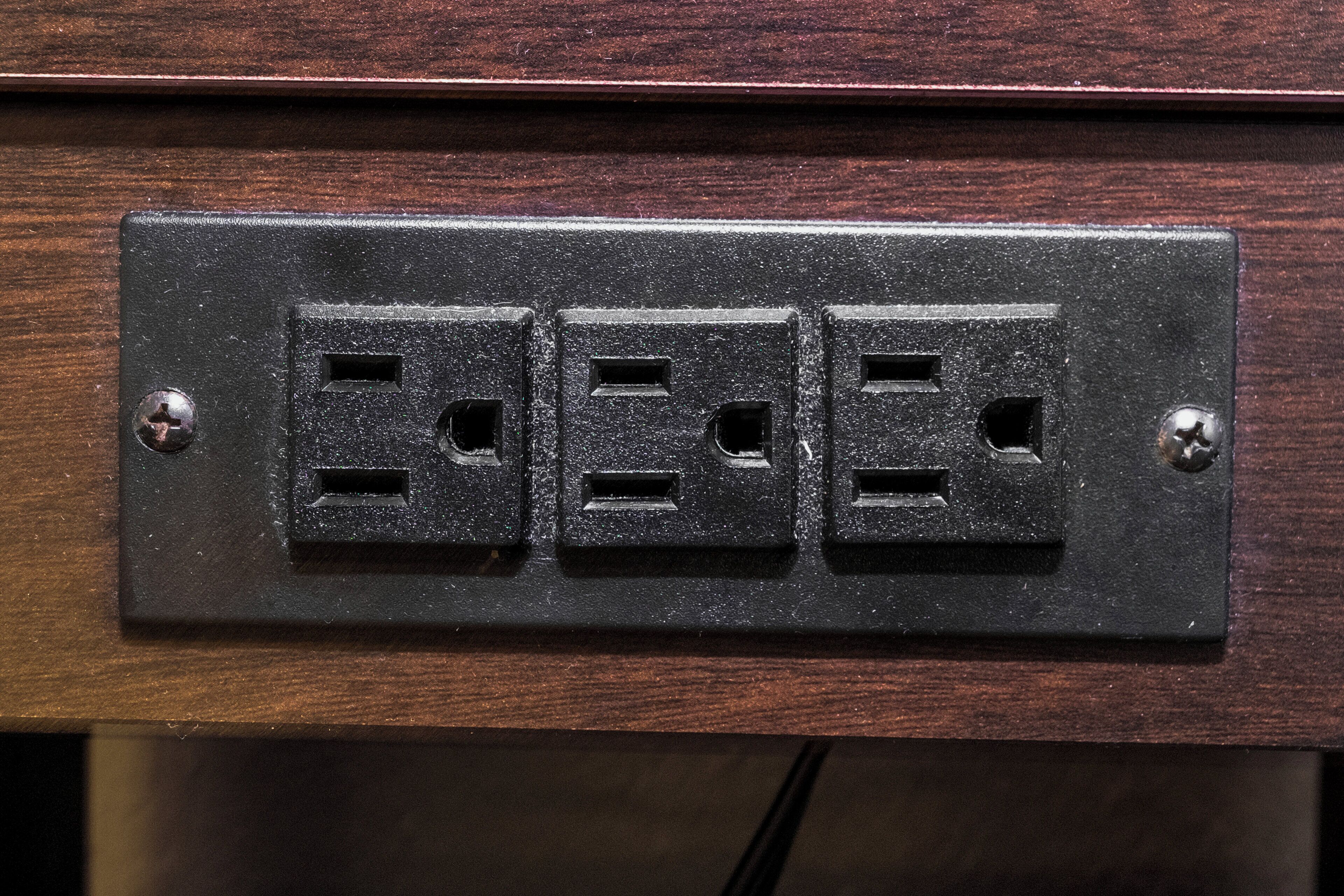 A black electrical outlet with three sockets on a wooden surface.