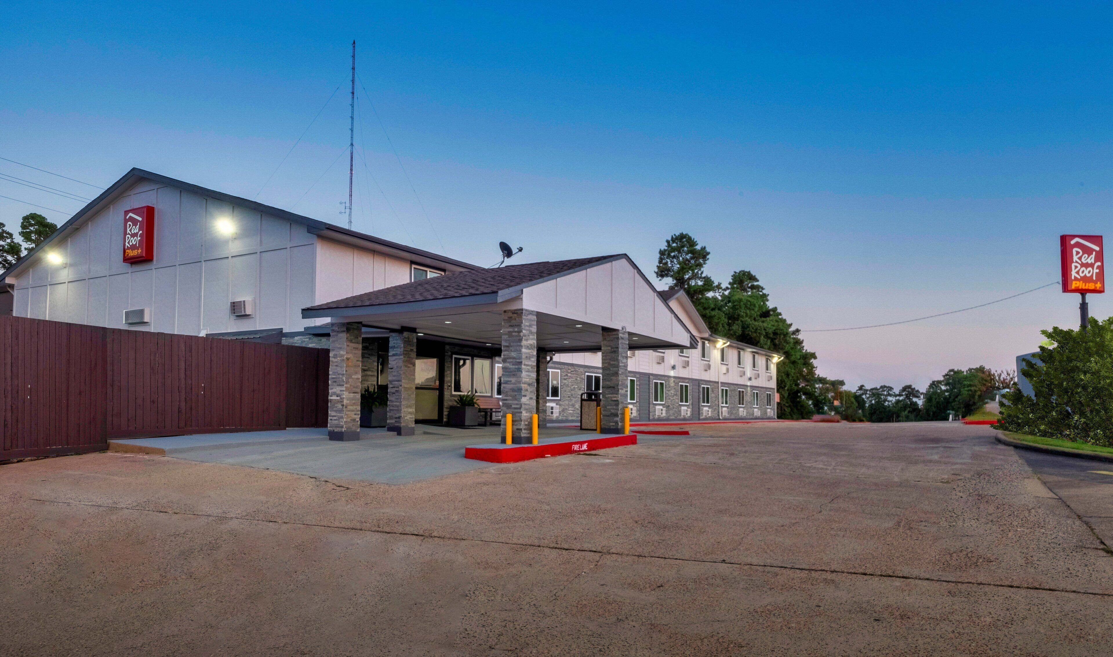 A Red Roof Plus hotel with a covered outdoor area and a parking lot.