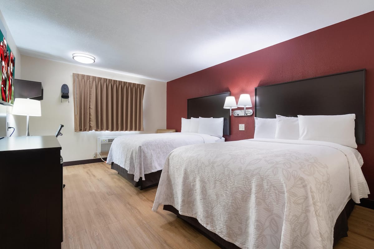 Ett hotellrum med två sängar, ett skrivbord, en lampa och en TV som är monterad på väggen.