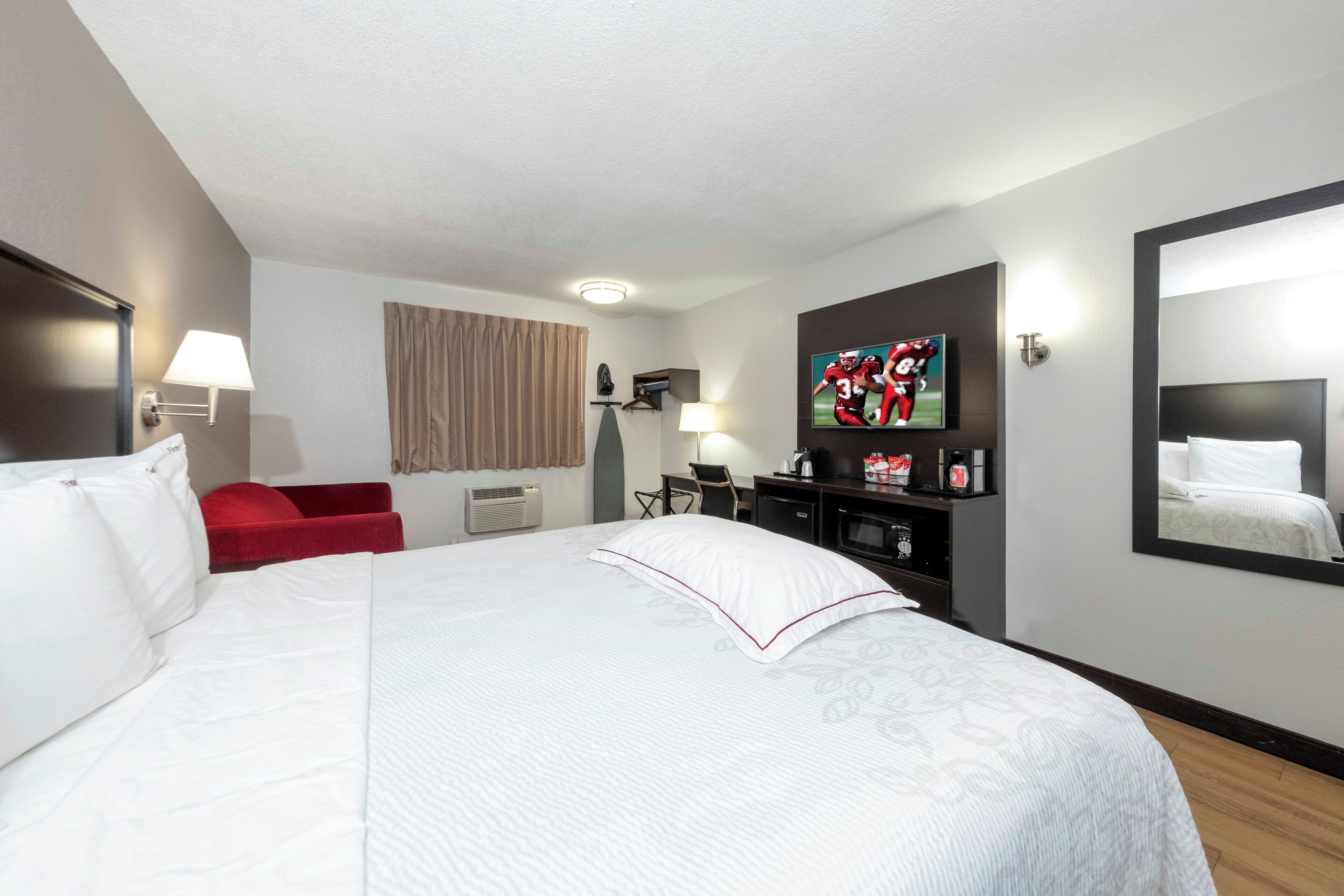 A hotel room with a large bed, a desk, a chair, a television, and a mirror.