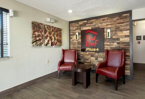 A reception area with two leather chairs, a small table, and a wall-mounted sign reading 'Red Roof Plus+'.