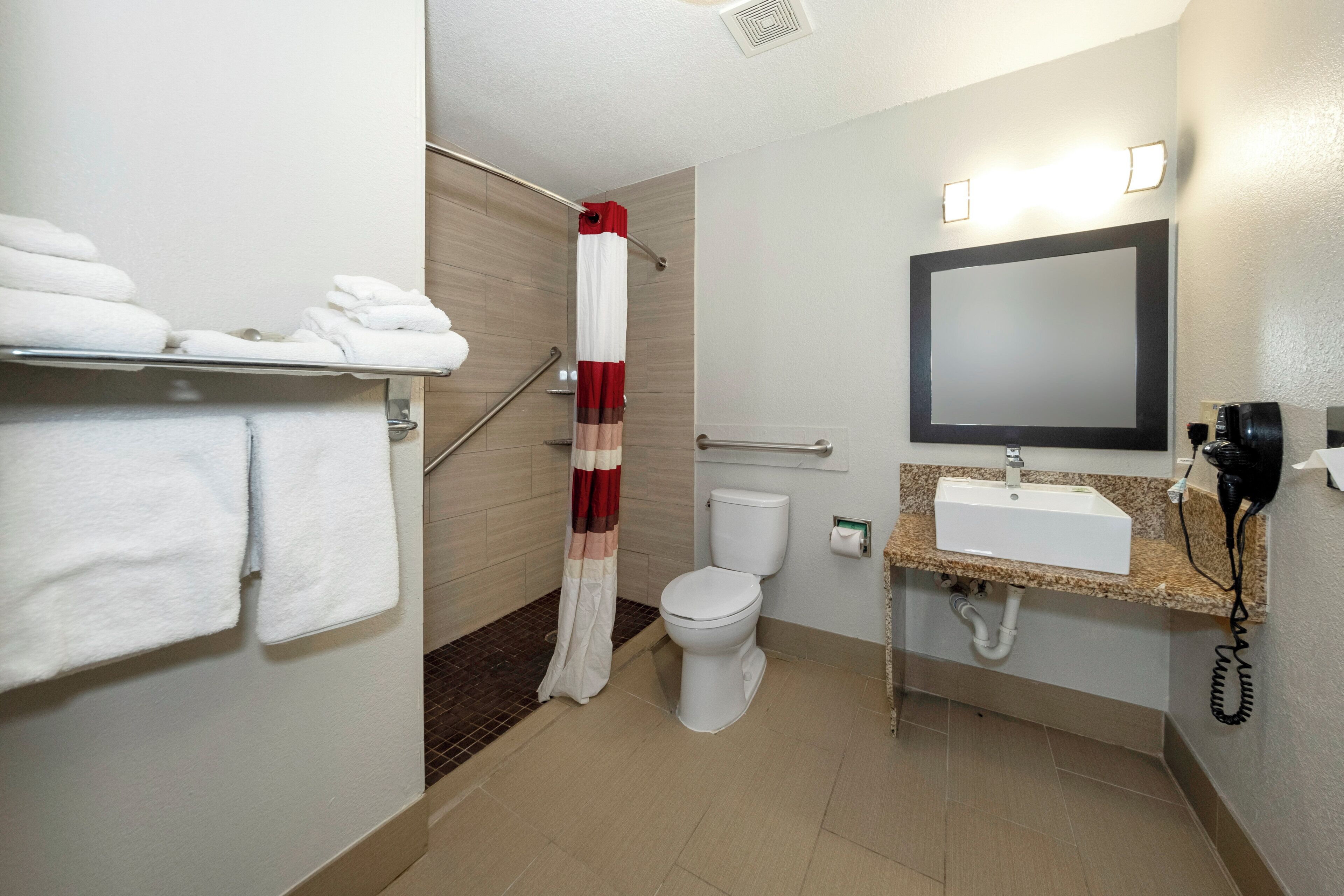 A hotel bathroom with a shower, toilet, sink, and towel rack.