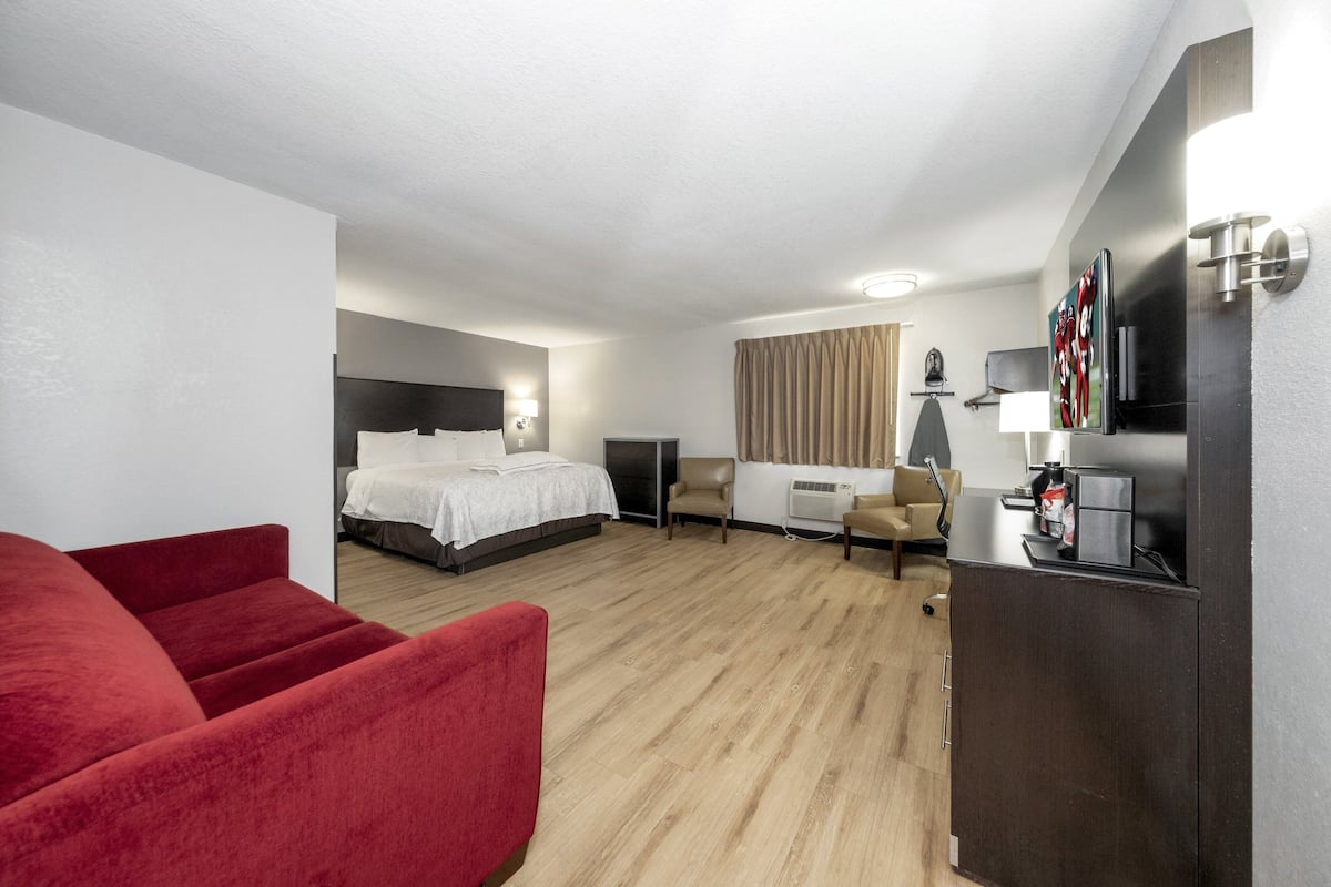 Ett hotellrum med en säng, ett skrivbord, en stol, en tv och en röd soffa.