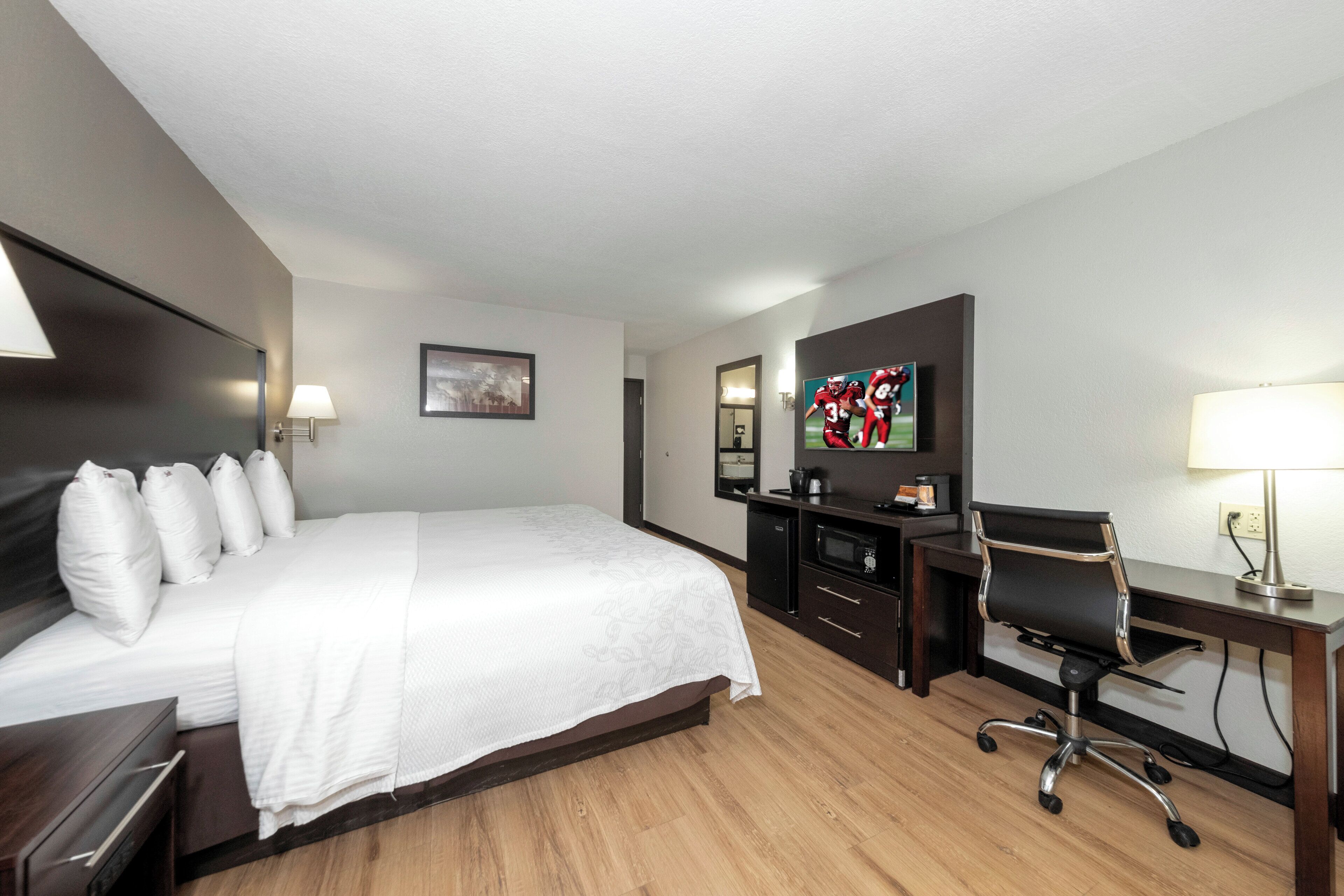 A hotel room with a bed, a desk, a chair, a television, and a lamp.