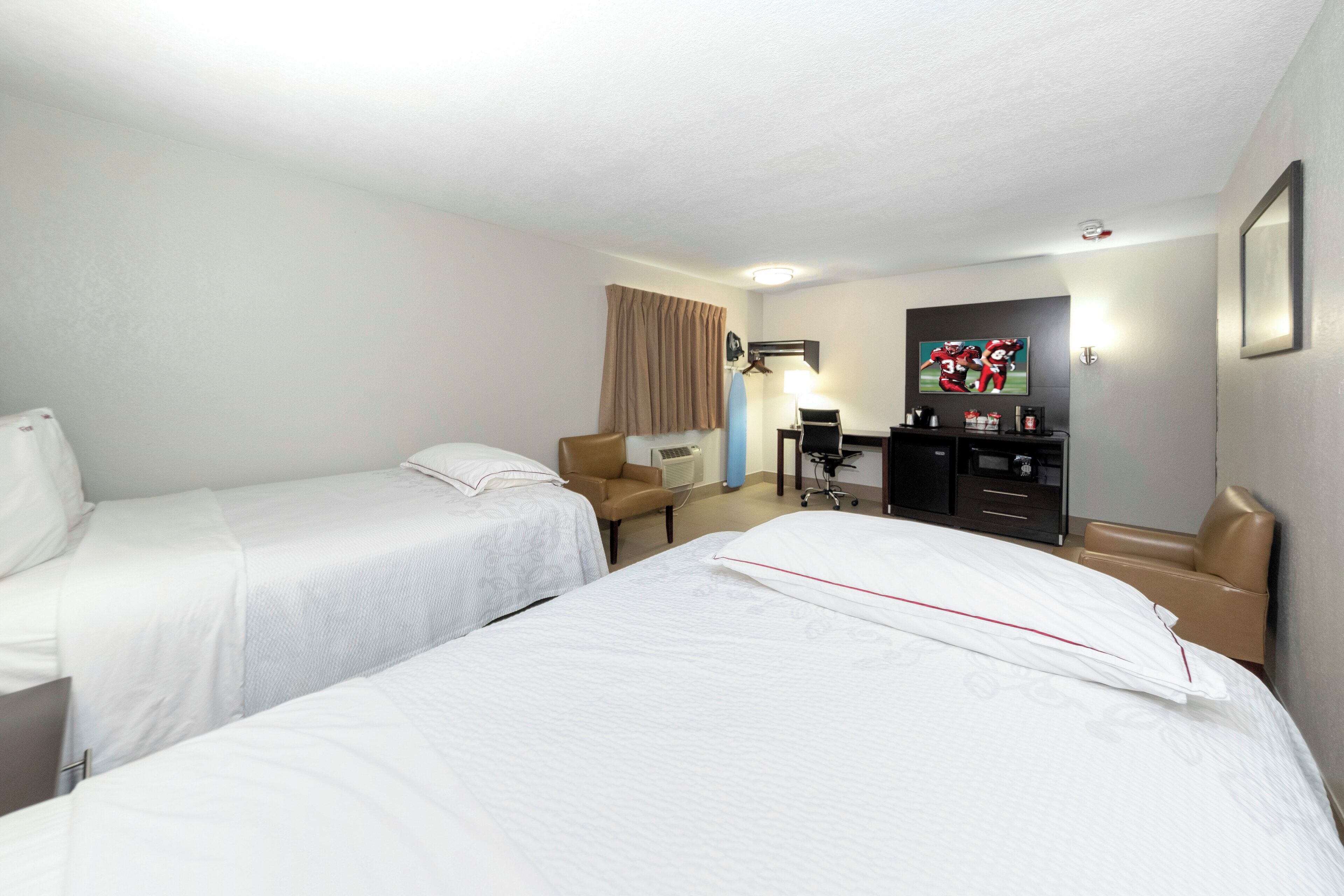 Quarto de hotel com duas camas de solteiro, uma escrivaninha com cadeira, televisão e guarda-roupa.