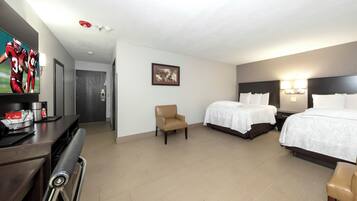 Habitación de hotel con dos camas, un escritorio con silla, un televisor y un cuadro en la pared.