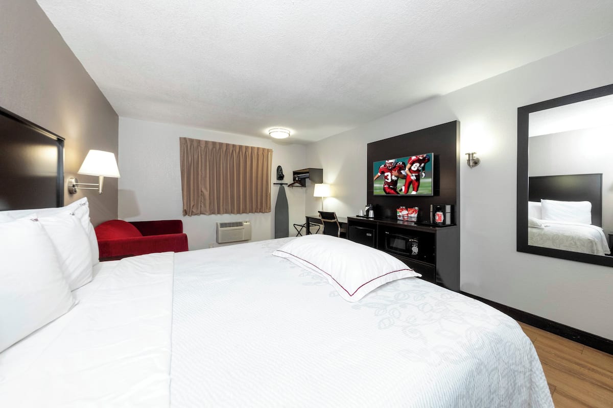 Ett hotellrum med en stor säng, ett skrivbord, en tv och en spegel.