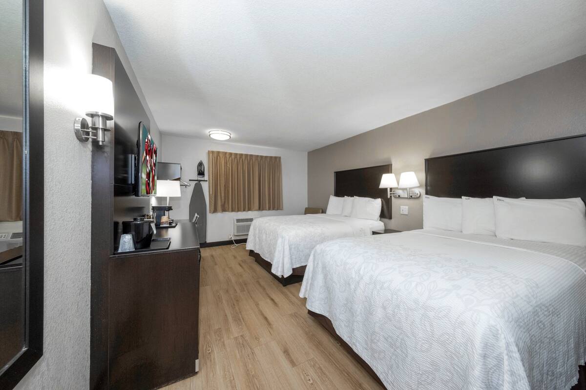 A hotel room with two beds, a desk with a coffee maker, a TV, and a large mirror.