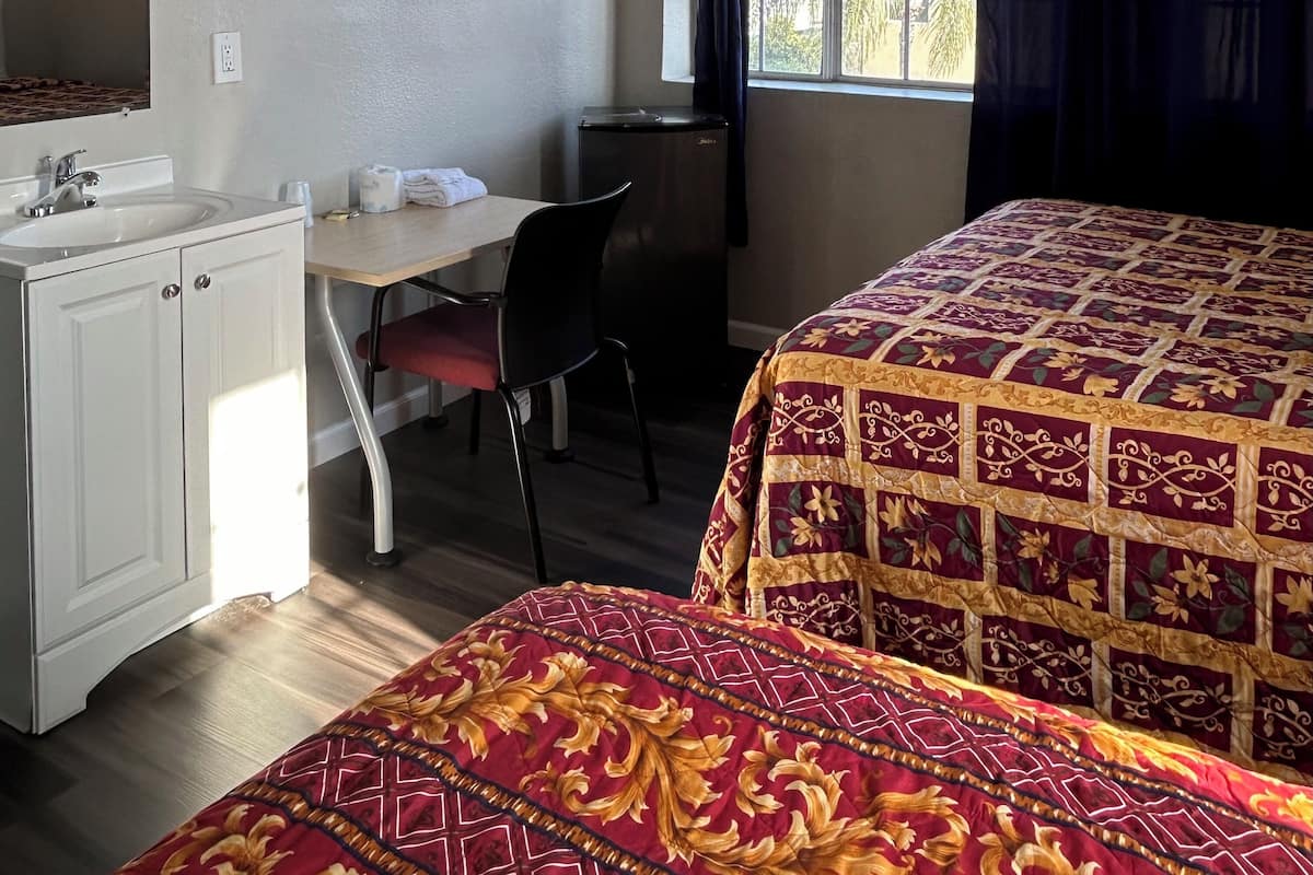 Habitació d'hotel amb llit, escriptori amb cadira, nevera petita i finestra amb cortines.