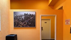 Un couloir orné d’une photographie représentant un paysage urbain, avec une poubelle et une porte sur laquelle est apposée une pancarte.