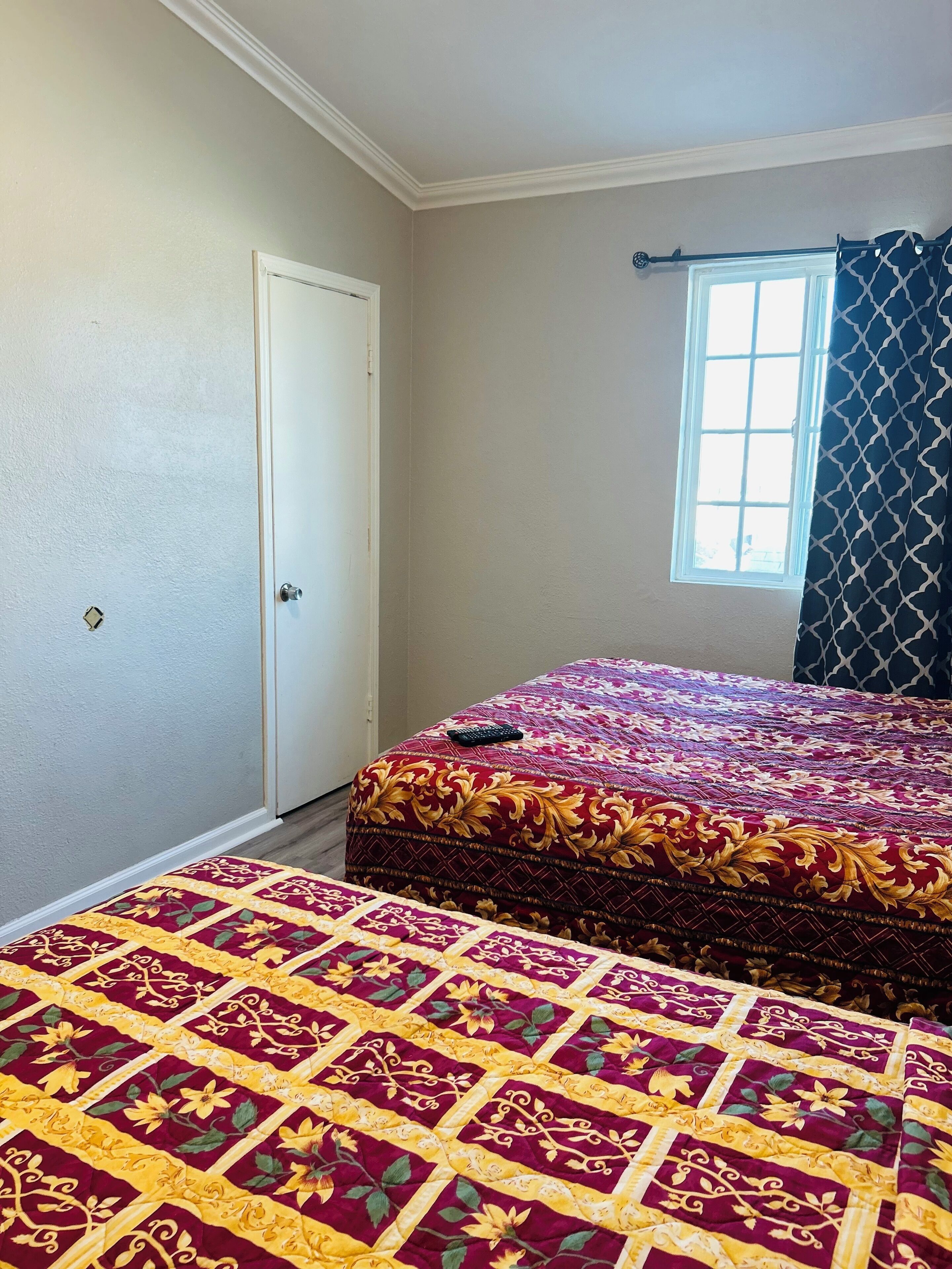 Une chambre avec un grand lit, une fenêtre ornée d’un rideau à motifs et une porte.