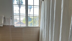 Une salle de bain avec une fenêtre, un rideau de douche blanc et des murs carrelés.