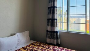 Une chambre à coucher avec un lit, une fenêtre donnant sur des immeubles et un rideau.