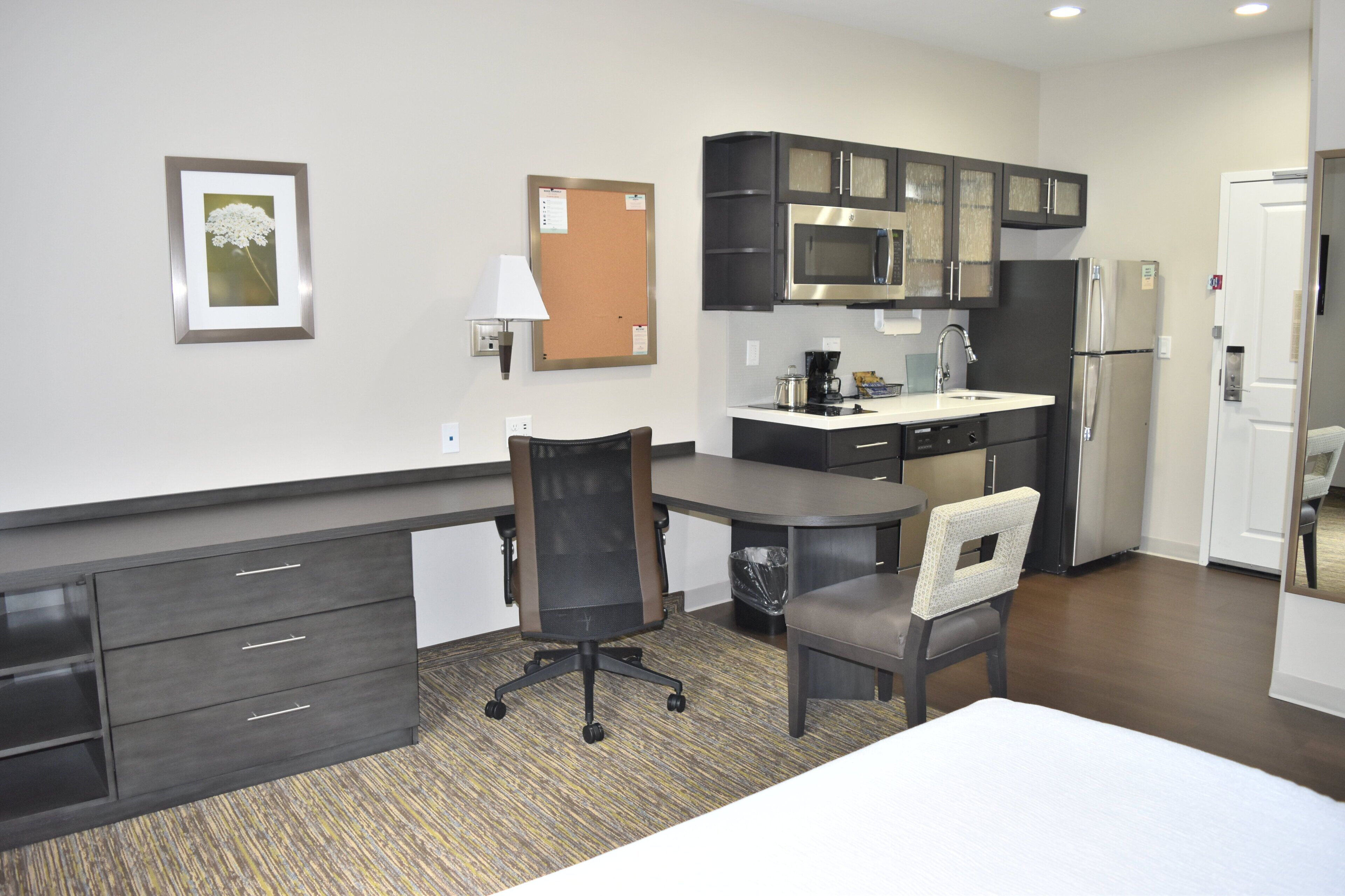 Una habitación de hotel con cama, escritorio, silla, kitchenette y baño.