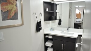 A modern bathroom with a white sink, black cabinets, and a framed leaf artwork on the wall.