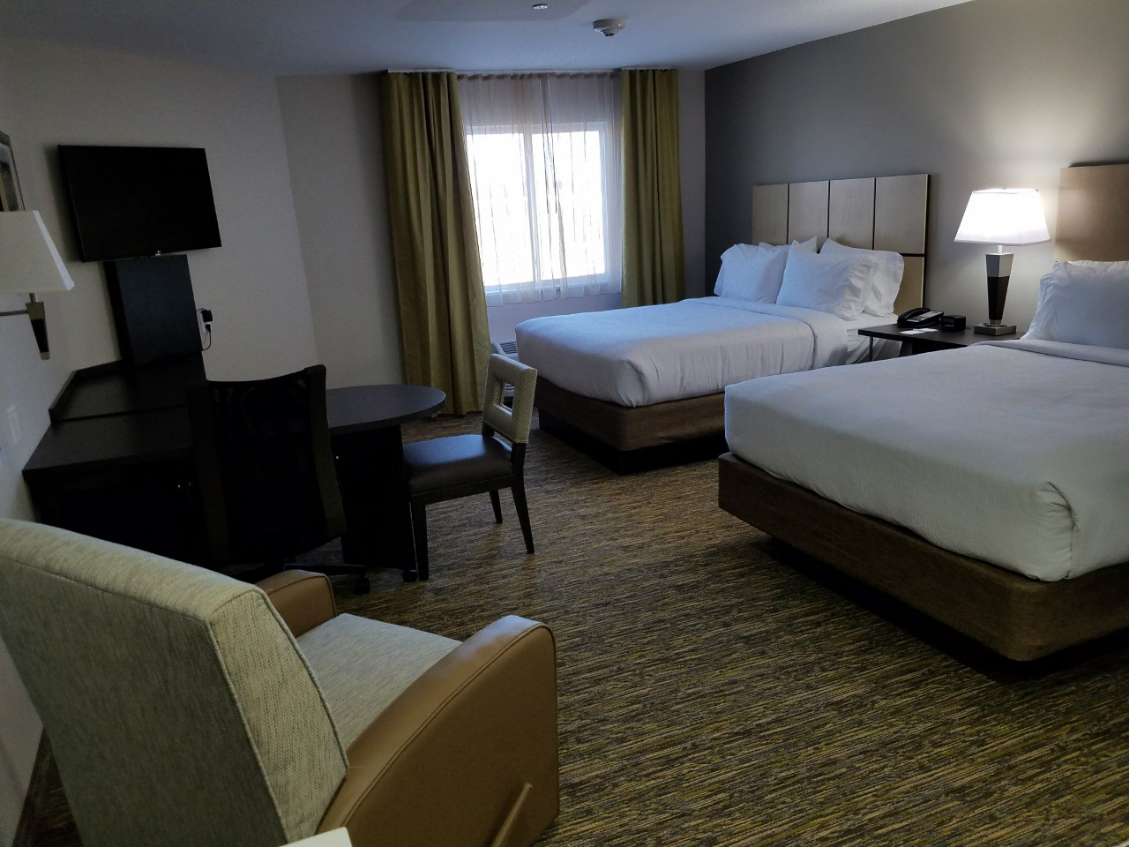 A hotel room with two beds, a desk, a chair, a television, and a lamp.