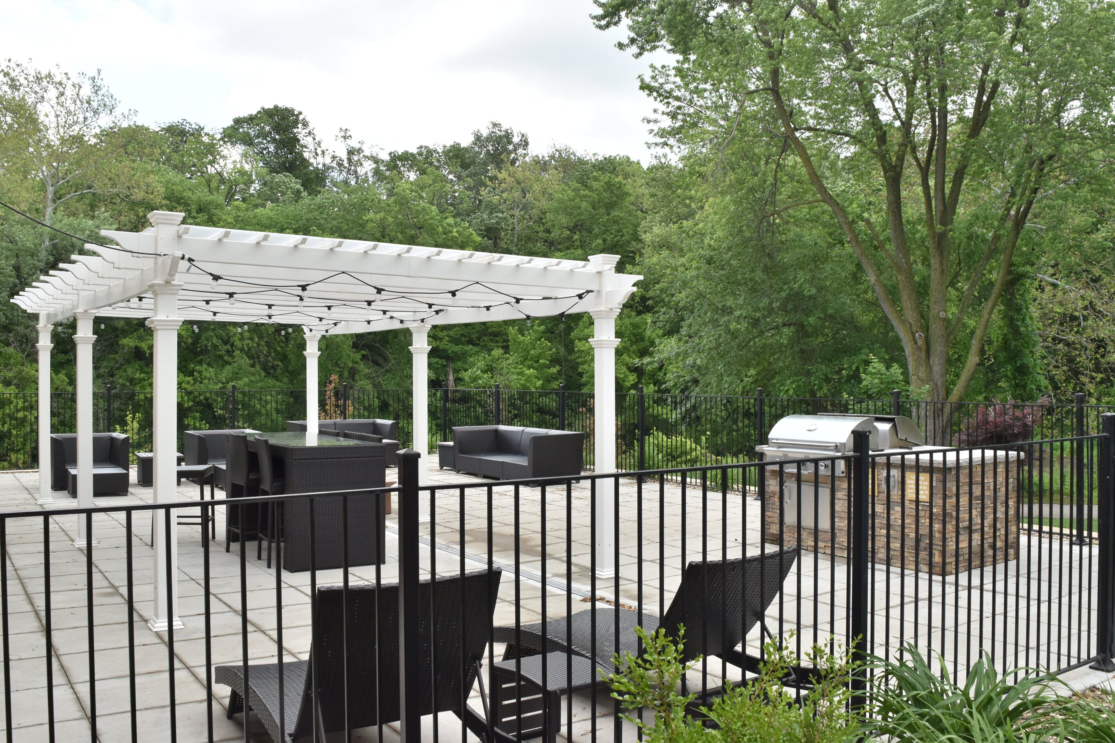 An outdoor patio with a pergola, seating, and a grill area.