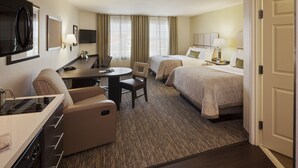 A hotel room with a kitchenette, two beds, a dining table, and a TV.