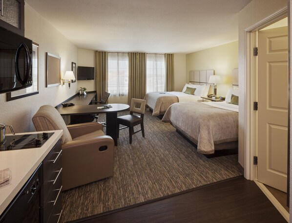 A hotel room with a kitchenette, two beds, a dining table, and a TV. - Candlewood Suites Kansas City - Independence by IHG (Independence)