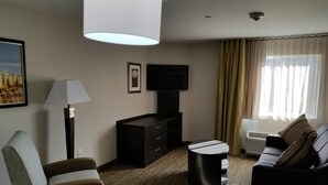 A modern hotel room with a sofa, a coffee table, a TV, a lamp, and a large window with curtains.