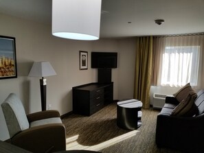 A modern hotel room with a sofa, a coffee table, a TV, a lamp, and a large window with curtains. - Candlewood Suites Kansas City - Independence by IHG (Independence)