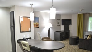A modern hotel room with a dining area, a sofa, a TV, and a flat-screen TV mounted on the wall.