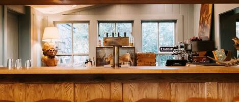 A bar area with wooden paneling, a counter with stools, and a view of the outdoors through windows.