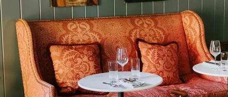 A dining area with a sofa, two round tables, and wall-mounted paintings.