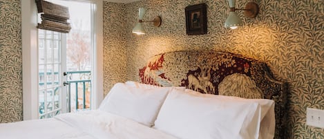 A bedroom with a large bed, patterned wallpaper, a decorative headboard, and a window with a view of the outside.