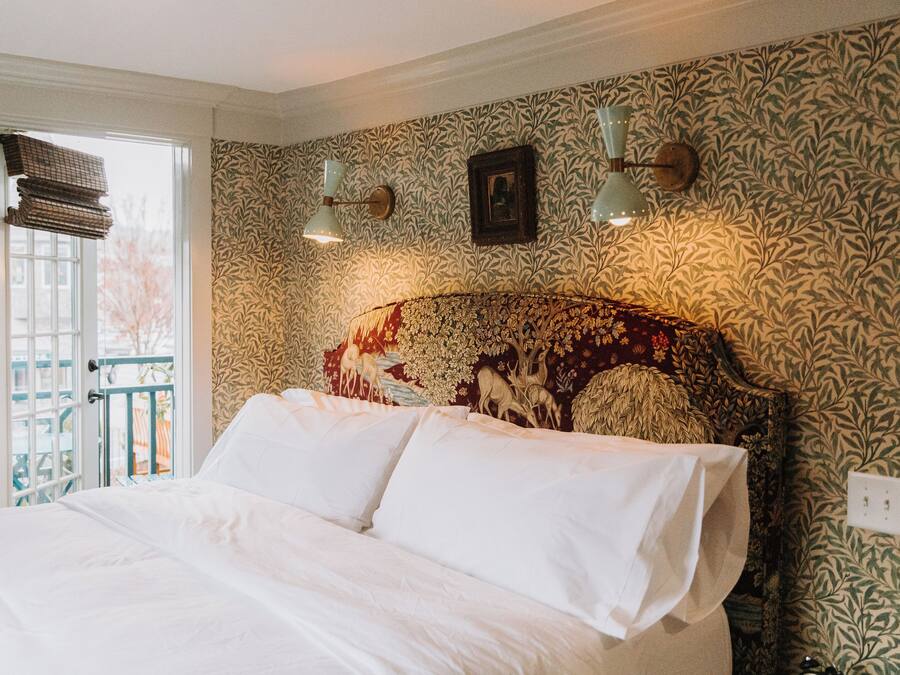 A bedroom with a large bed, patterned wallpaper, a decorative headboard, and a window with a view of the outside.