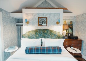 A bedroom with a bed, a bedside table, a dresser, and a wall with patterned wallpaper.