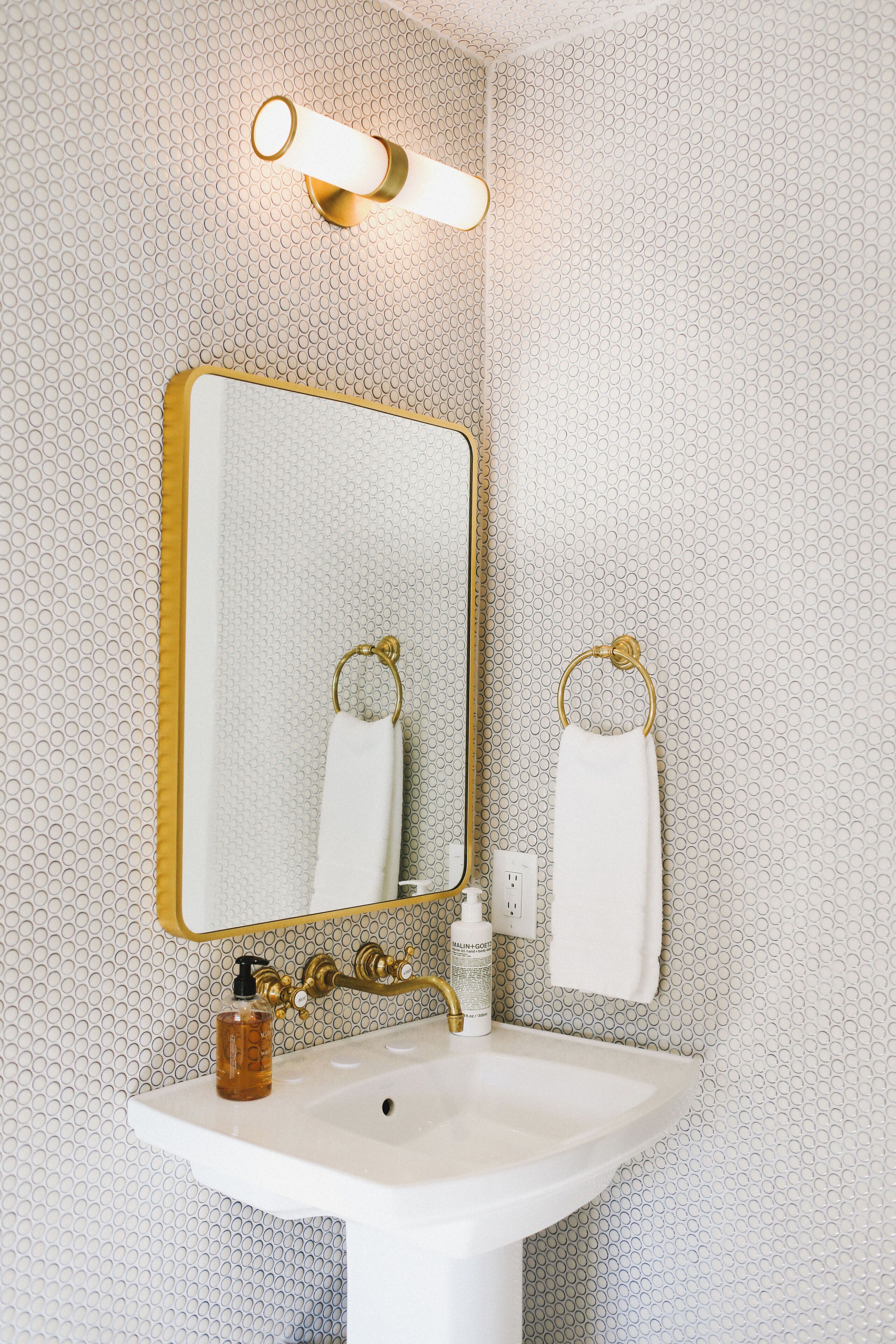 A bathroom with a white sink, gold fixtures, and a patterned wall.