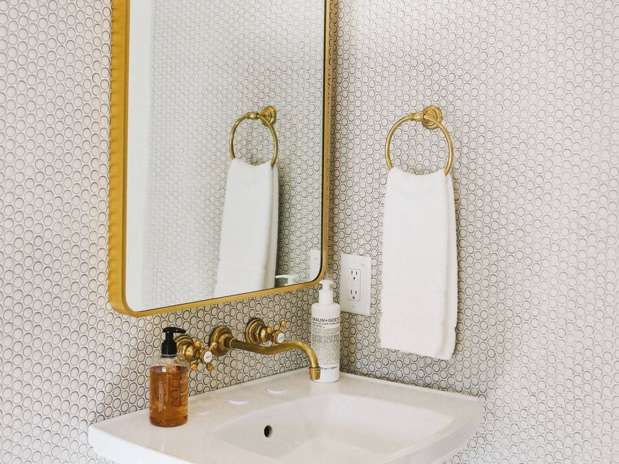 A bathroom with a white sink, gold fixtures, and a patterned wall.