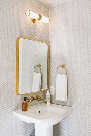 A bathroom with a white sink, gold fixtures, and a patterned wall.