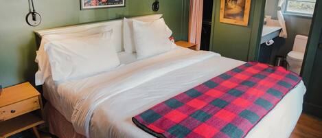 A neatly made bed with a checkered blanket, a framed poster on the wall, and a window with curtains.