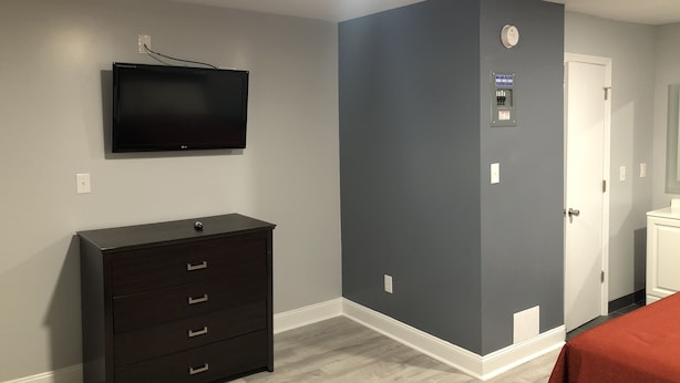 Una habitación con televisión de pantalla plana montada en la pared, un aparador de madera oscura, una pared de acento gris, una puerta con panel de control y una colcha roja.